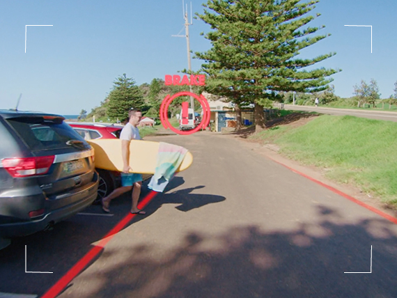 Man walking behind a car with a rear parking sensor.