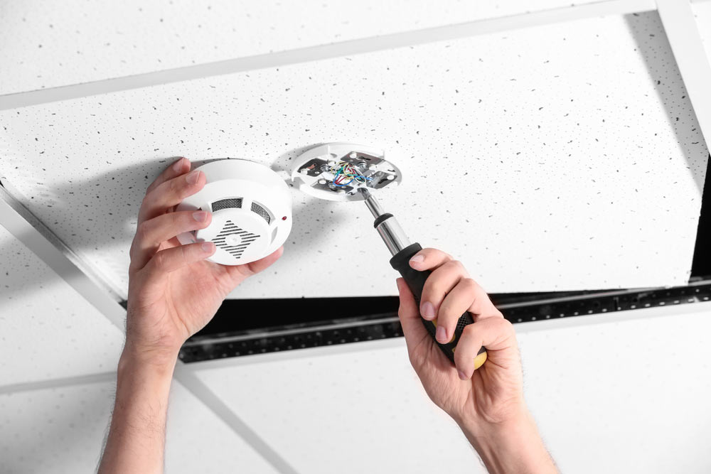 An electrician installing a smoke alarm on a commercial ceiling