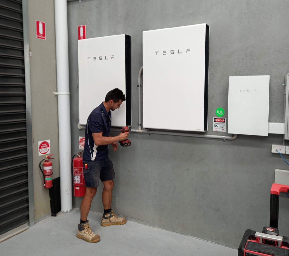 An electrician installing a Tesla Power Wall on a commercial building in Rowville