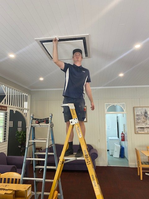 An electrician servicing a commercial air conditioner vent in a building on the Sunshine Coast